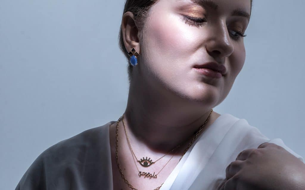 woman under the light wearing an earring and three necklaces inspired from the arab culture
